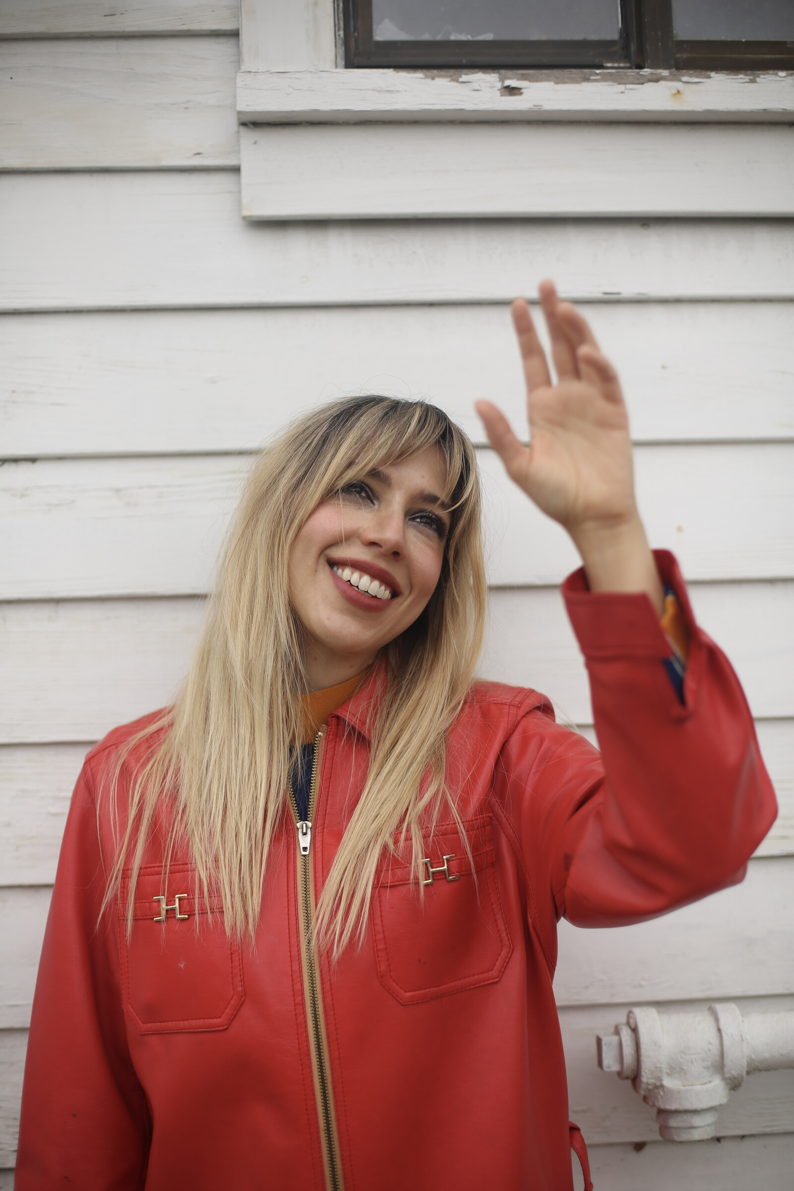Red jacket against the white clapboard, hand raised